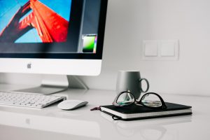 Desk with computer, glasses, notebook.